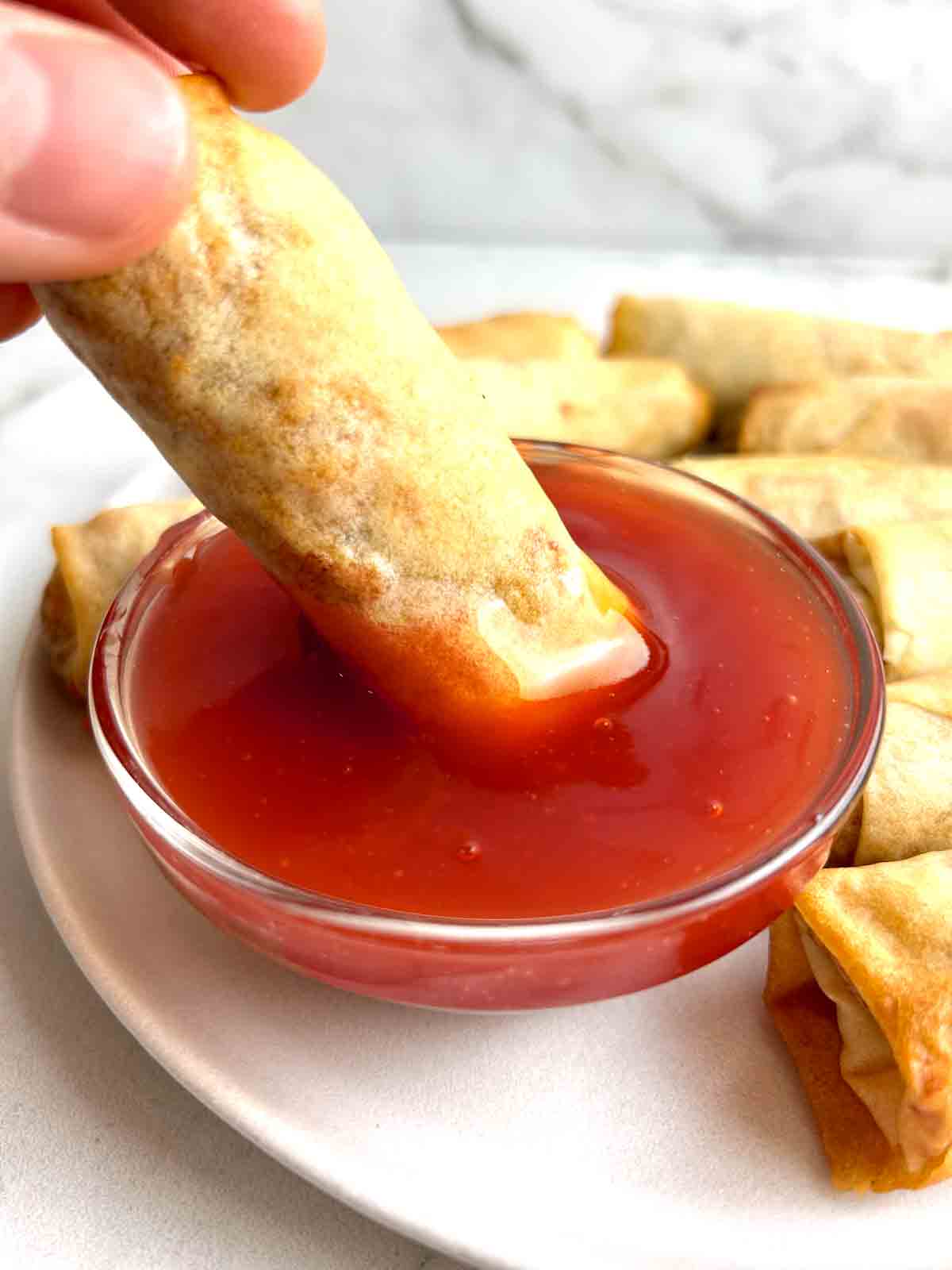 spring roll being dipped into sweet and sour sauce.