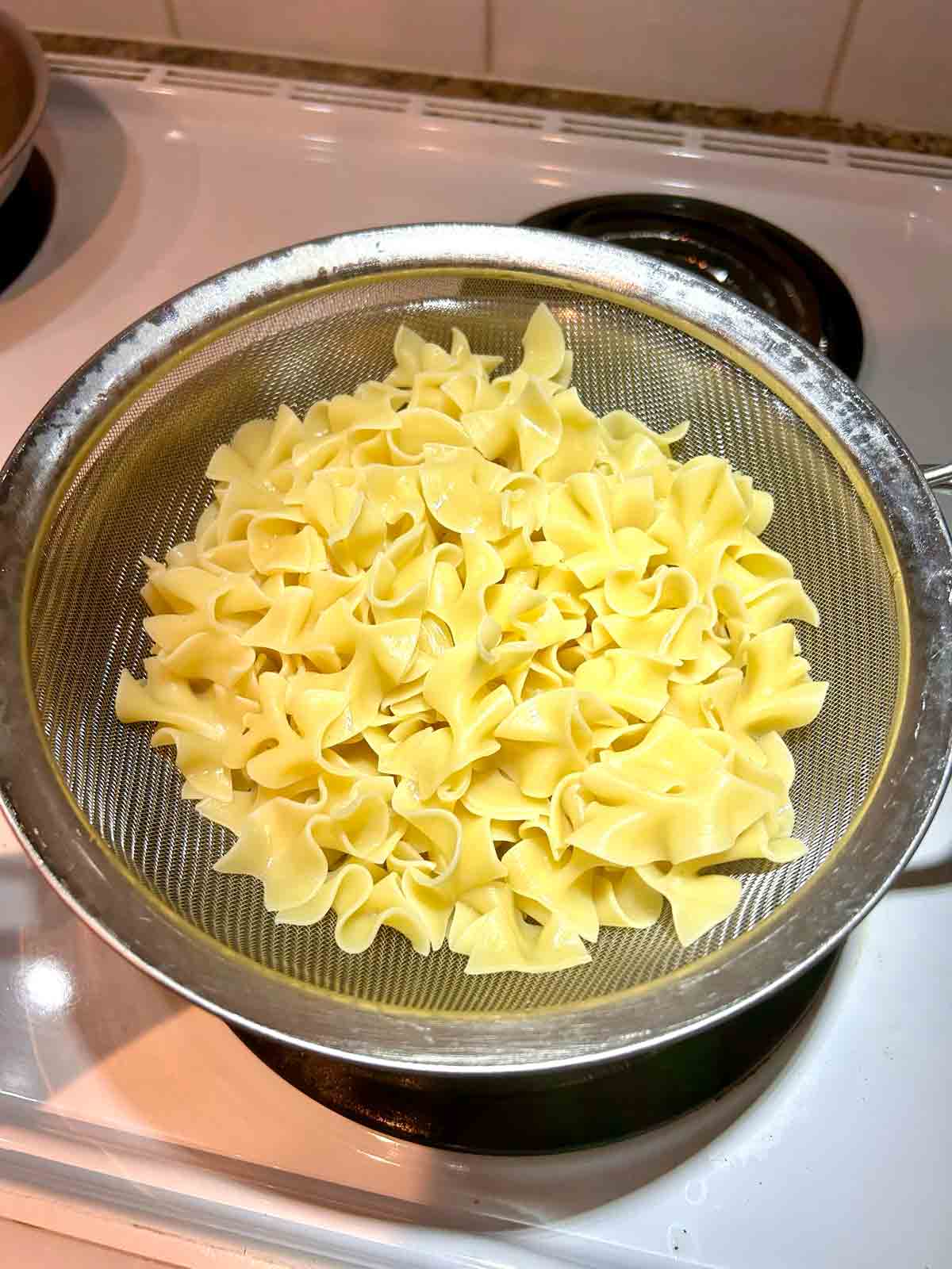 cooked egg noodles draining in colander.