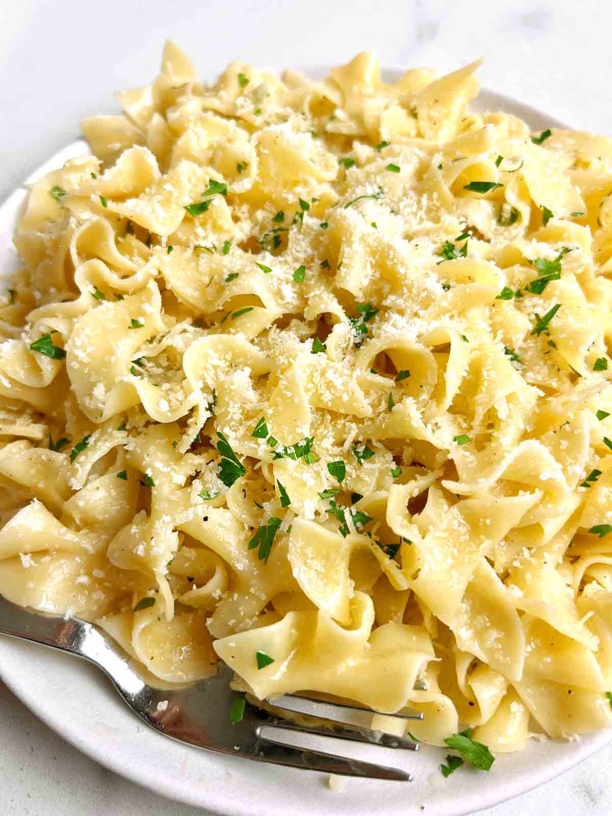 close up of buttered noodles with extra Parmesan sprinkled on top.