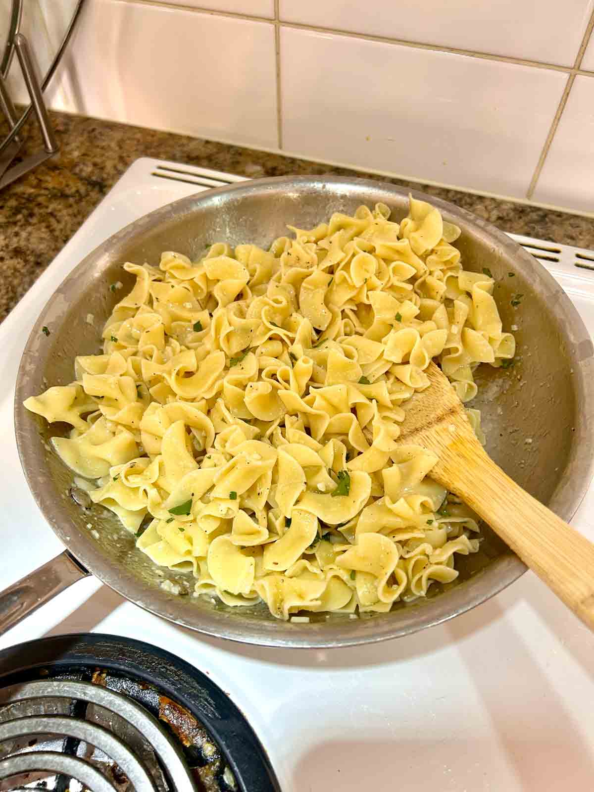 egg noodles tossed with butter sauce in pan.