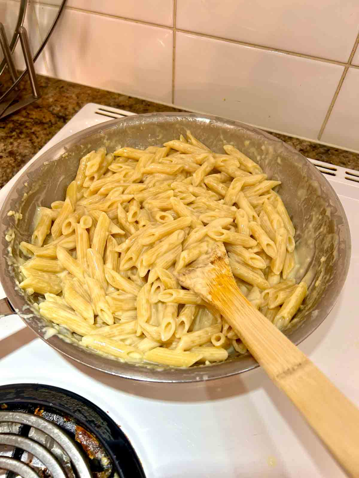 penne pasta tossed with sauce in pan.