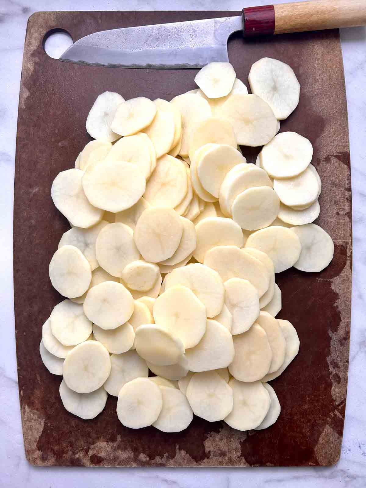 potatoes sliced thinly on cutting board.