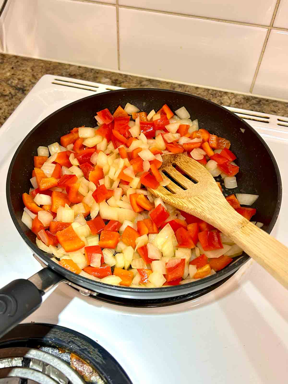 onions and red bell pepper being sautéed in pan.