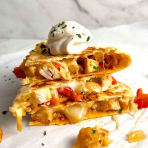 stack of quesadilla slices on top of each other with dollop of sour cream on top.