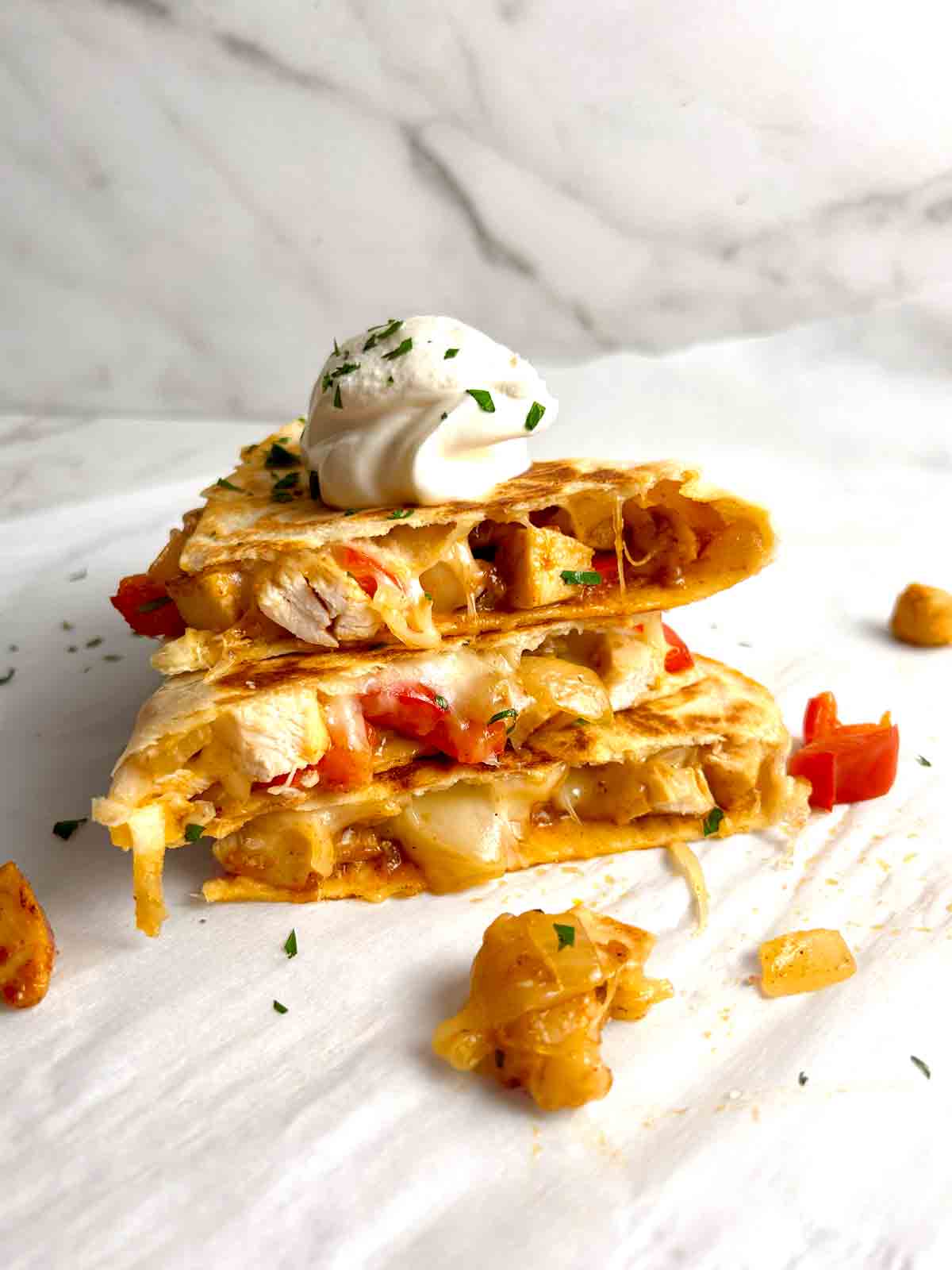 stack of quesadilla slices on top of each other with dollop of sour cream on top.