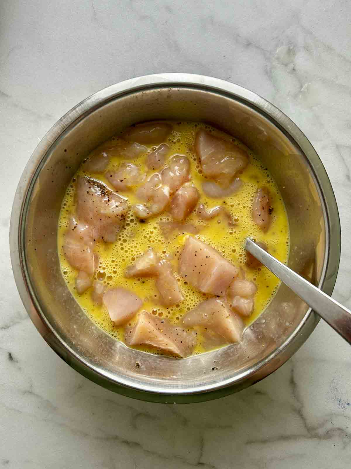 chicken cubes mixd with eggs and black pepper in bowl.