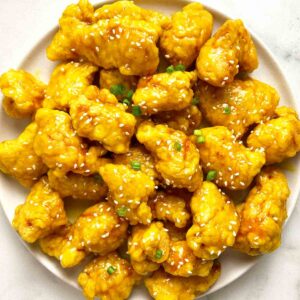 plate of Chinese lemon chicken with sesame seeds and green onions on top.