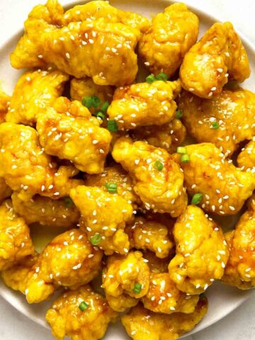 plate of Chinese lemon chicken with sesame seeds and green onions on top.