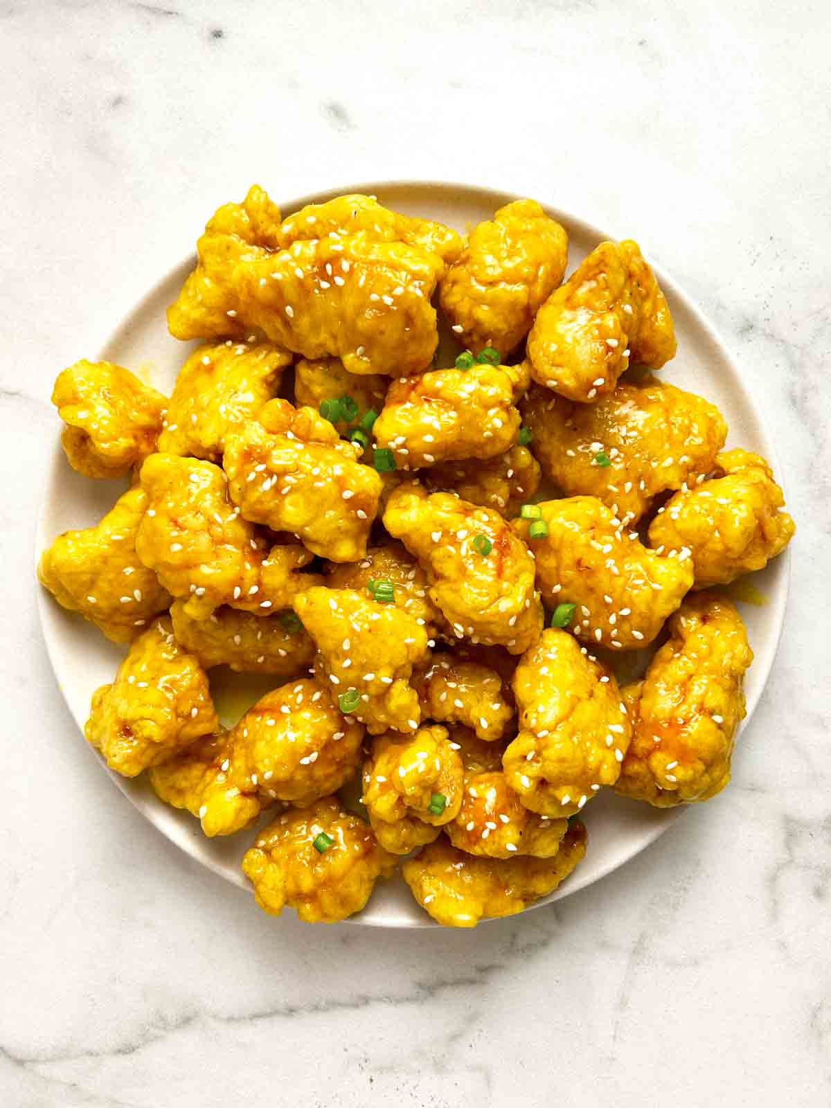 plate of Chinese lemon chicken with sesame seeds and green onions on top.