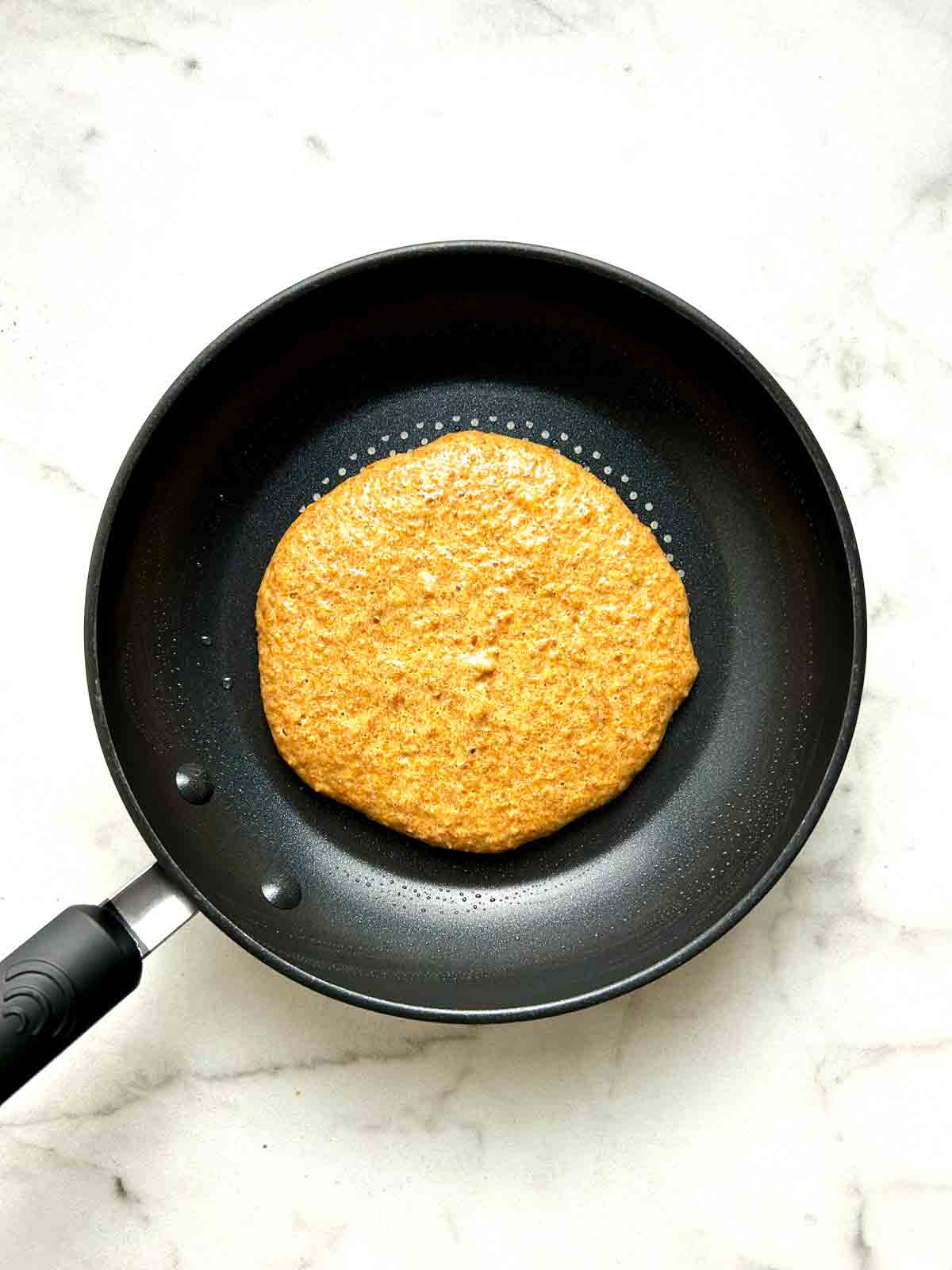 first side of pancake being cooked in pan.