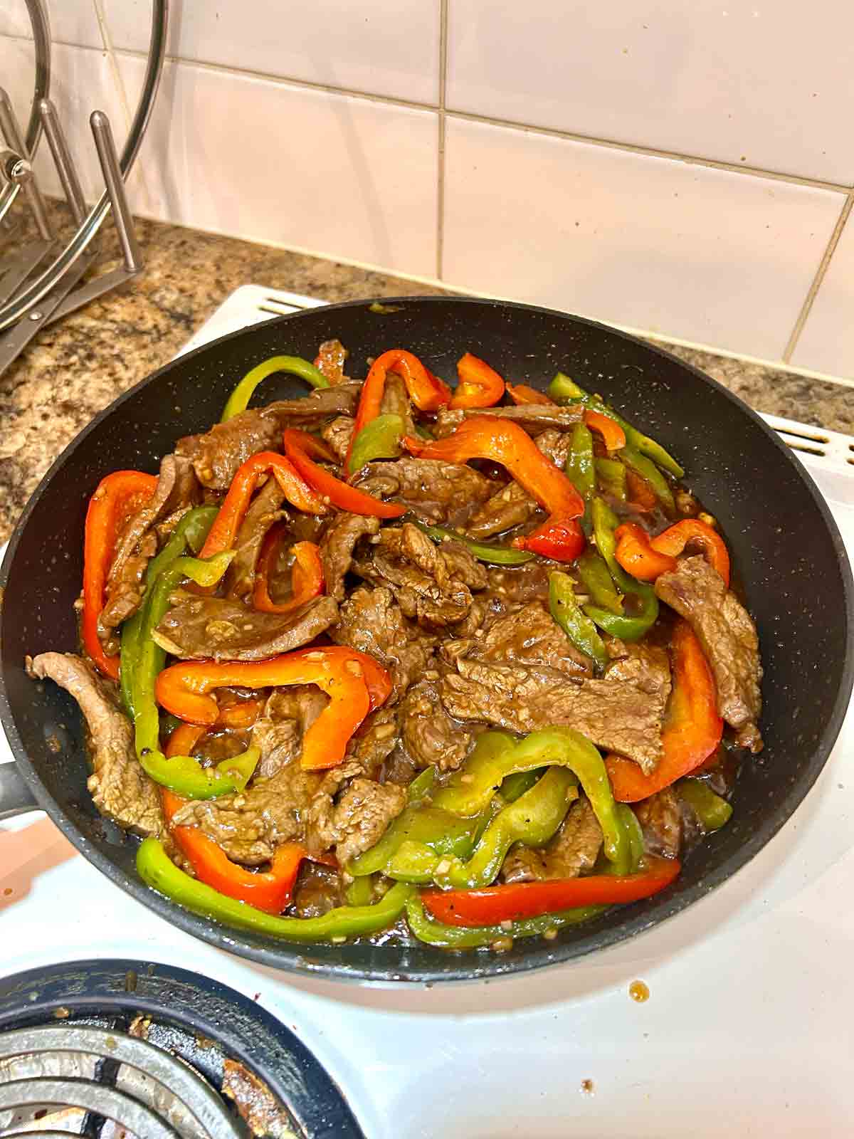 sauce thickened and tossed with beef and peppers in pan.