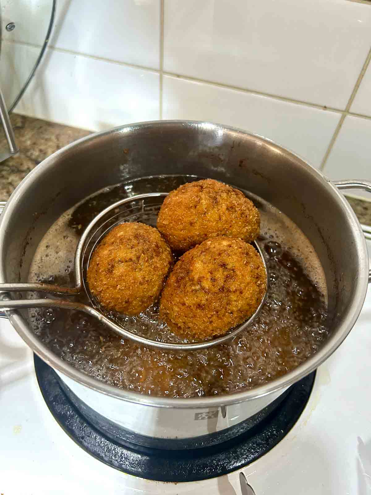scotch eggs being lifted out of hot oil.