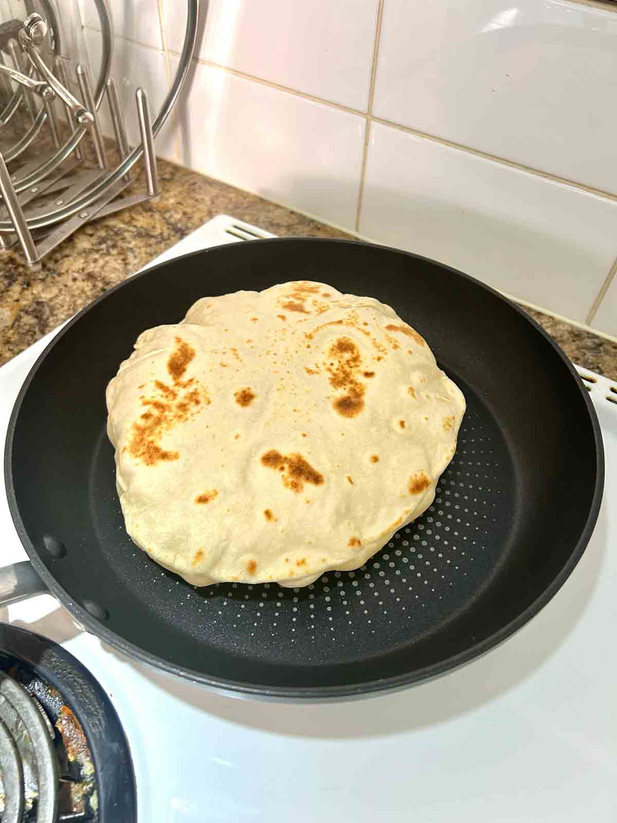 second side of tortilla cooking in skillet; noticeably puffed up.
