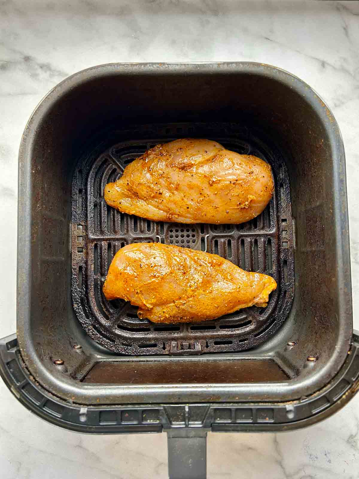 raw, seasoned chicken breasts in air fryer basket.