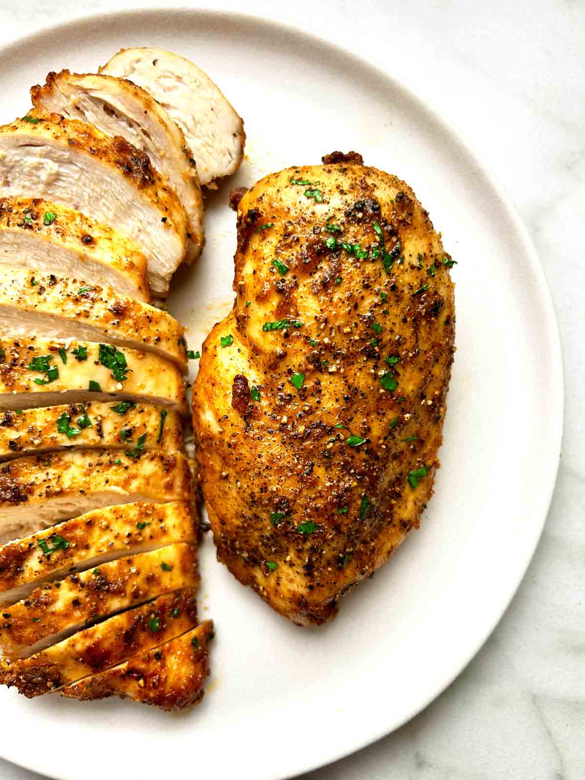 close up of air-fried chicken breasts on plate; one is sliced.
