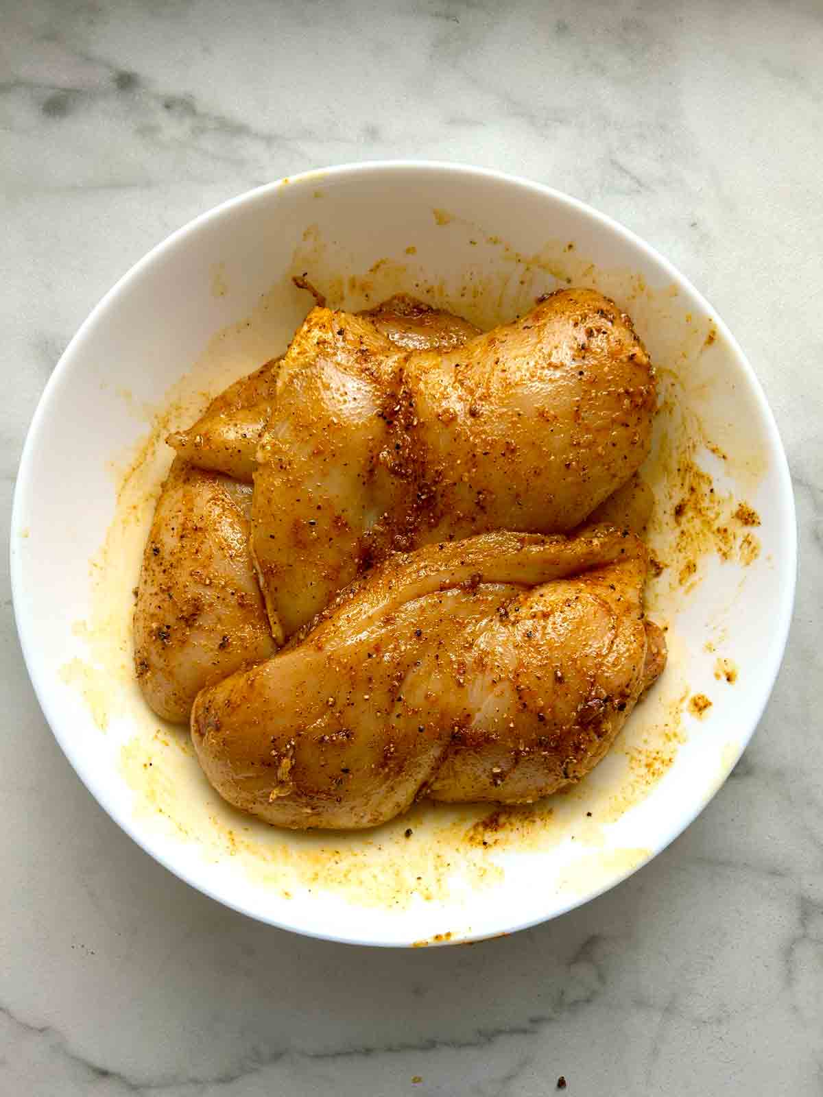 chicken breasts rubbed with spice mixture in bowl.