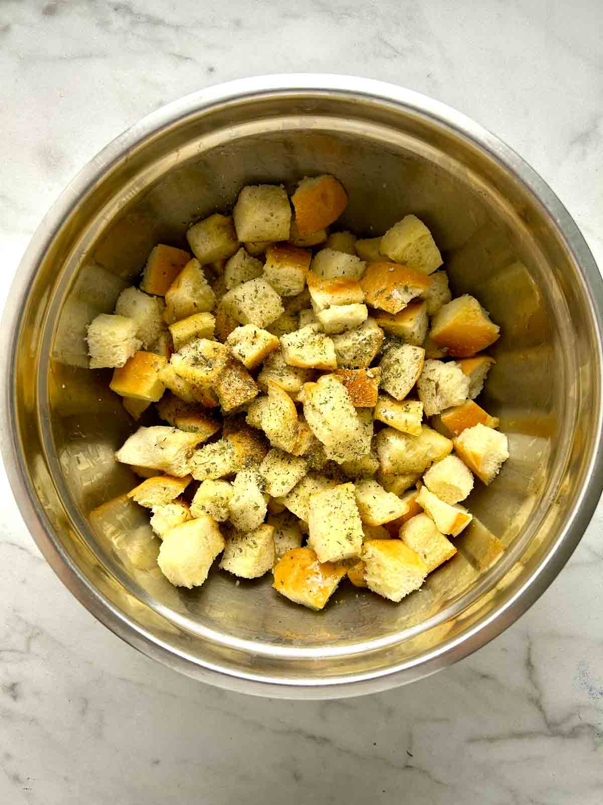 bread cubes tossed with seasonings in bowl.
