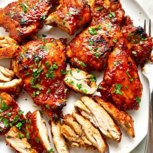 close up of barbecue boneless chicken thighs on plate; parsley garnished on top.