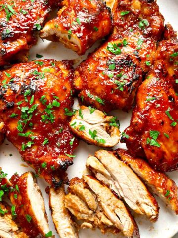 close up of barbecue boneless chicken thighs on plate; parsley garnished on top.