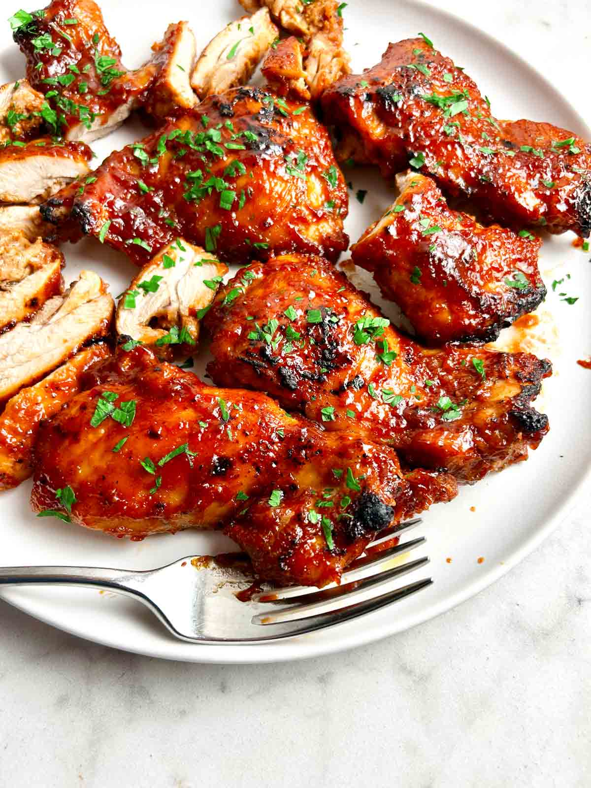 close up of barbecue boneless chicken thighs on plate; parsley garnished on top.