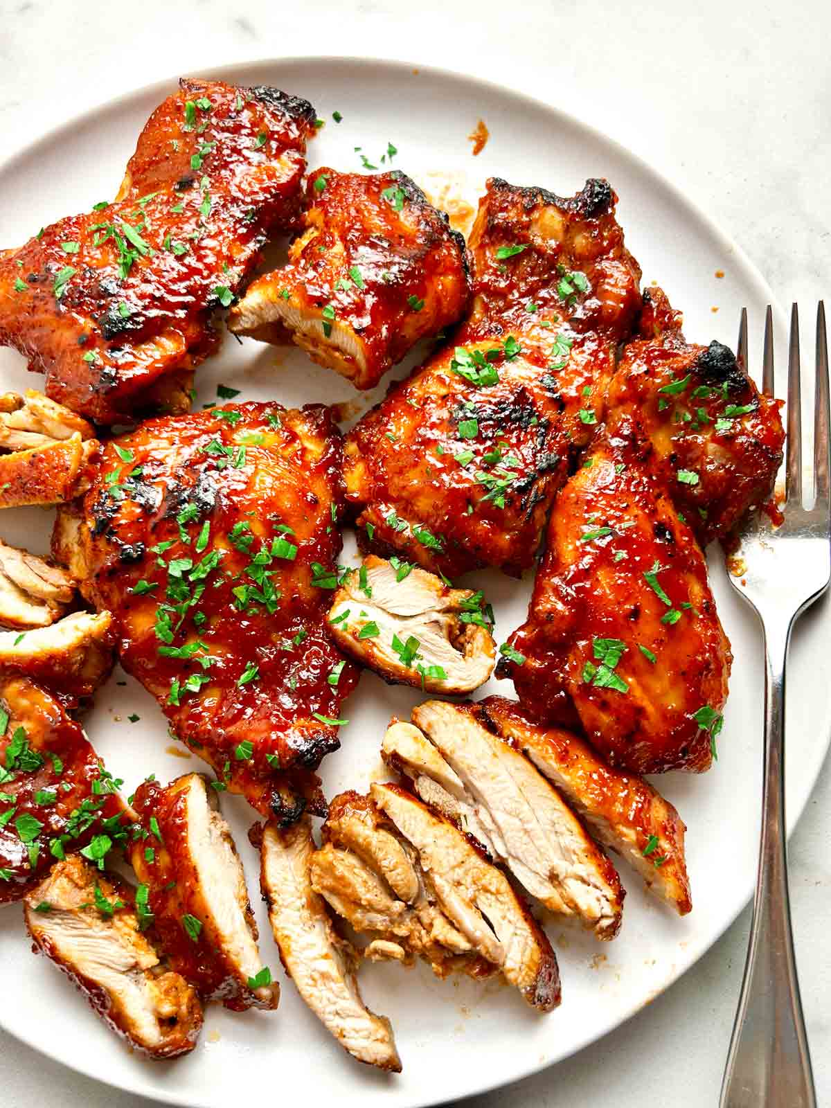 close up of barbecue boneless chicken thighs on plate; parsley garnished on top.