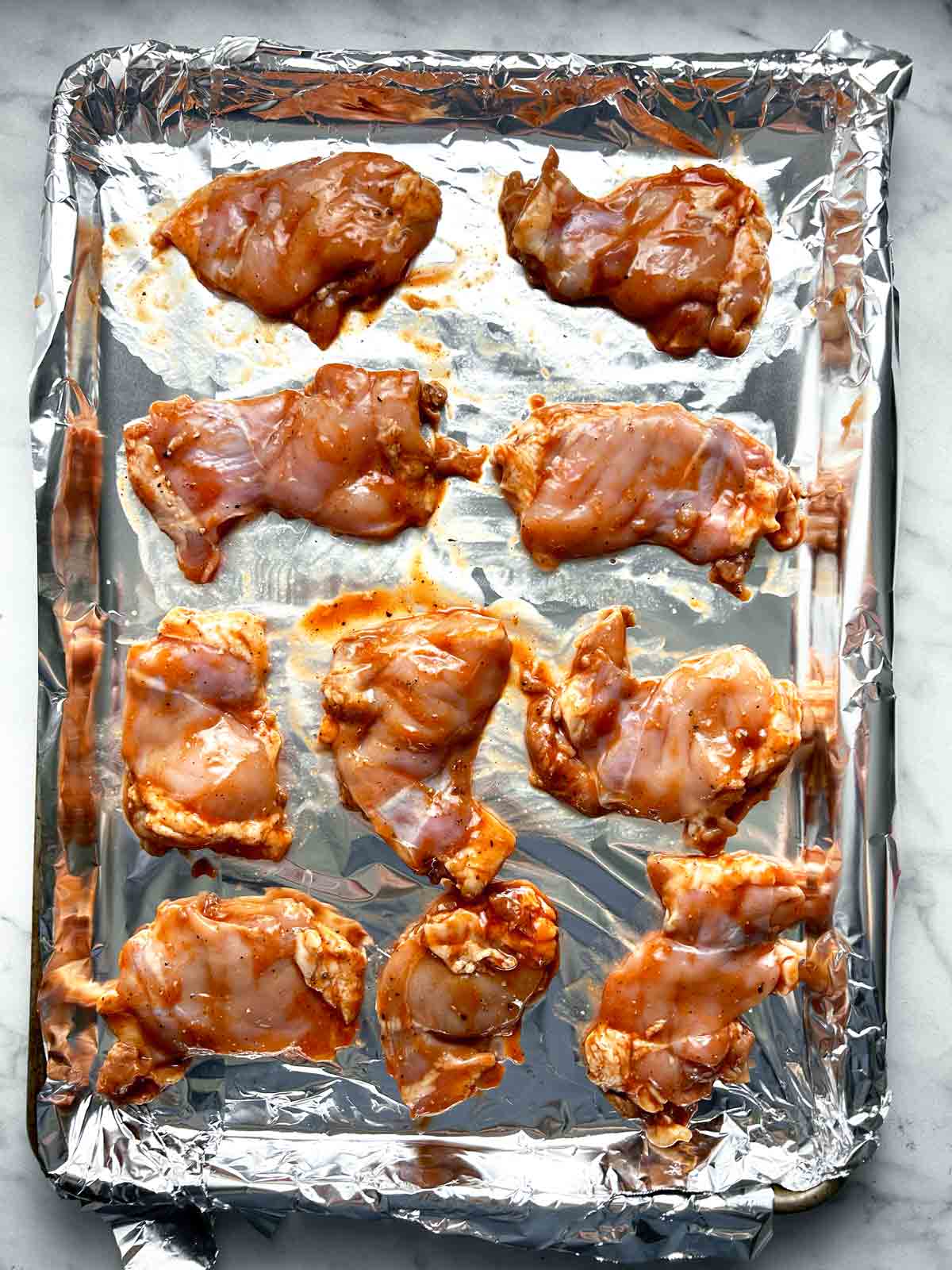 marinated chicken thighs spread on baking sheet lined with aluminum foil.