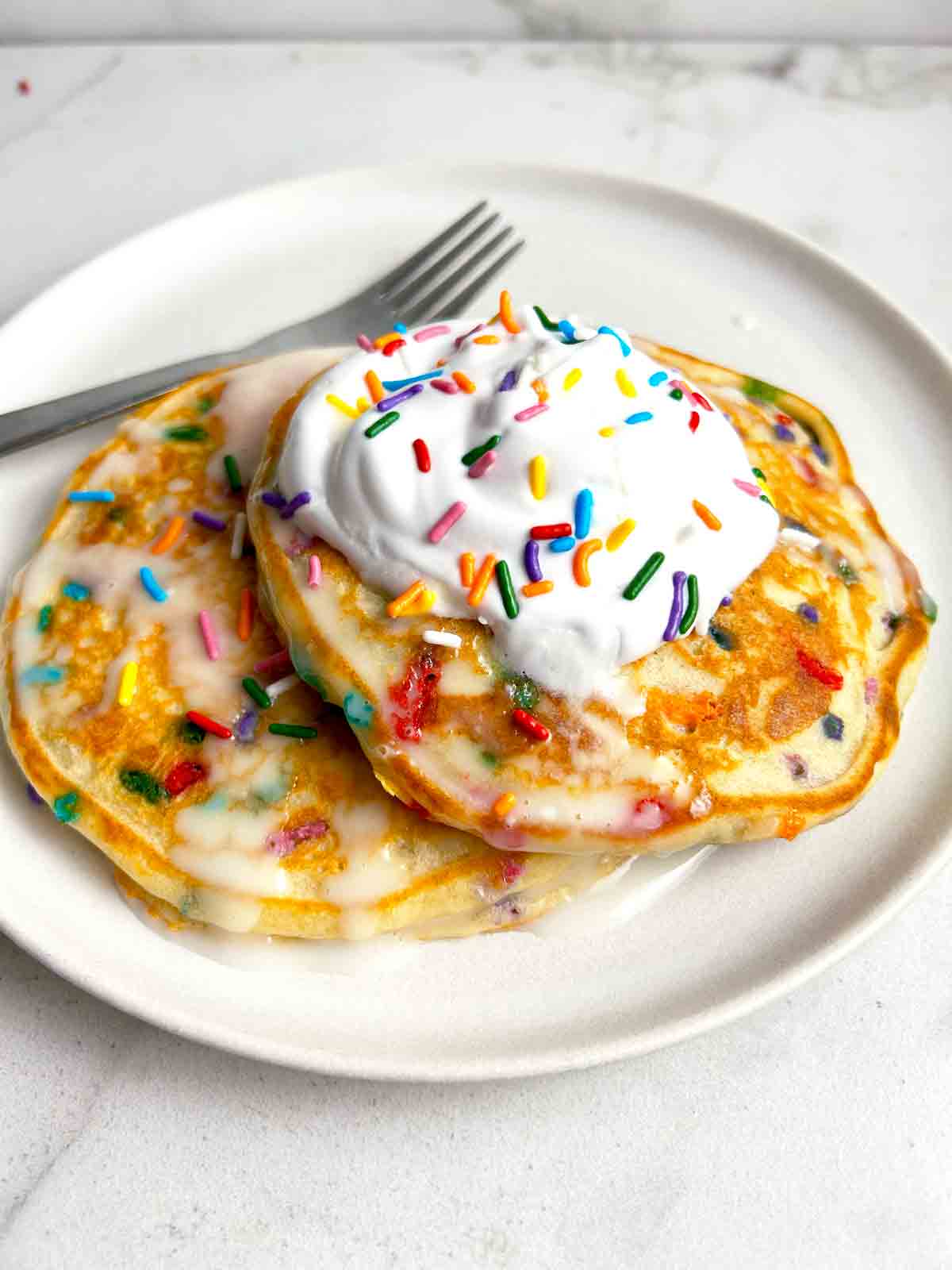 two birthday cake pancakes on plate with fork.