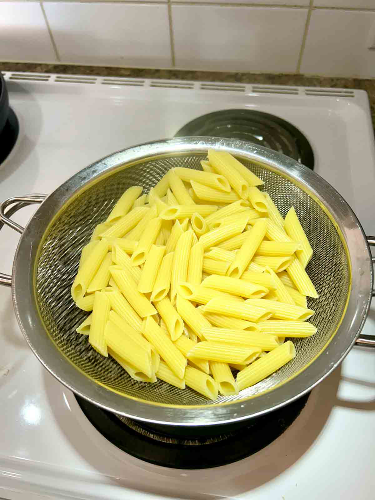 cooked penne draining over pot.