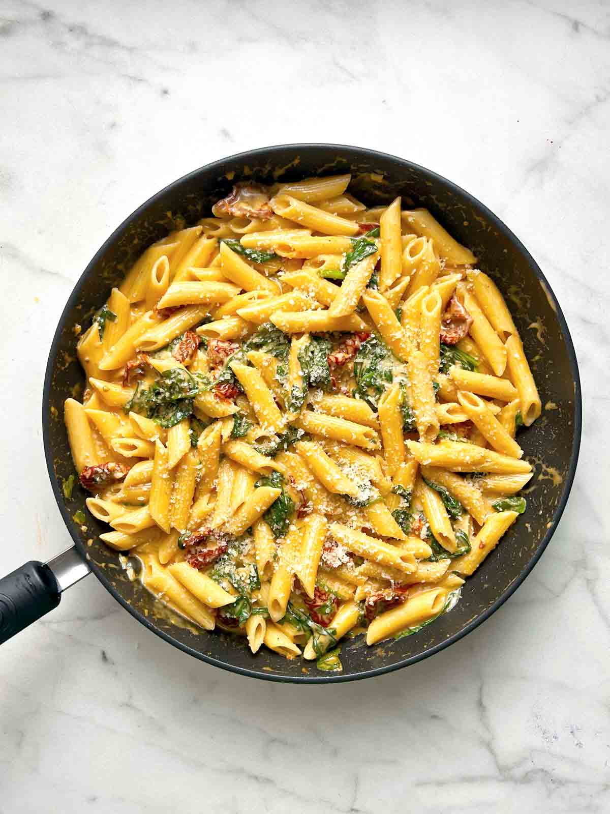 overhead shot of cooked pasta in pan; grated parmesan sprinkled on top.