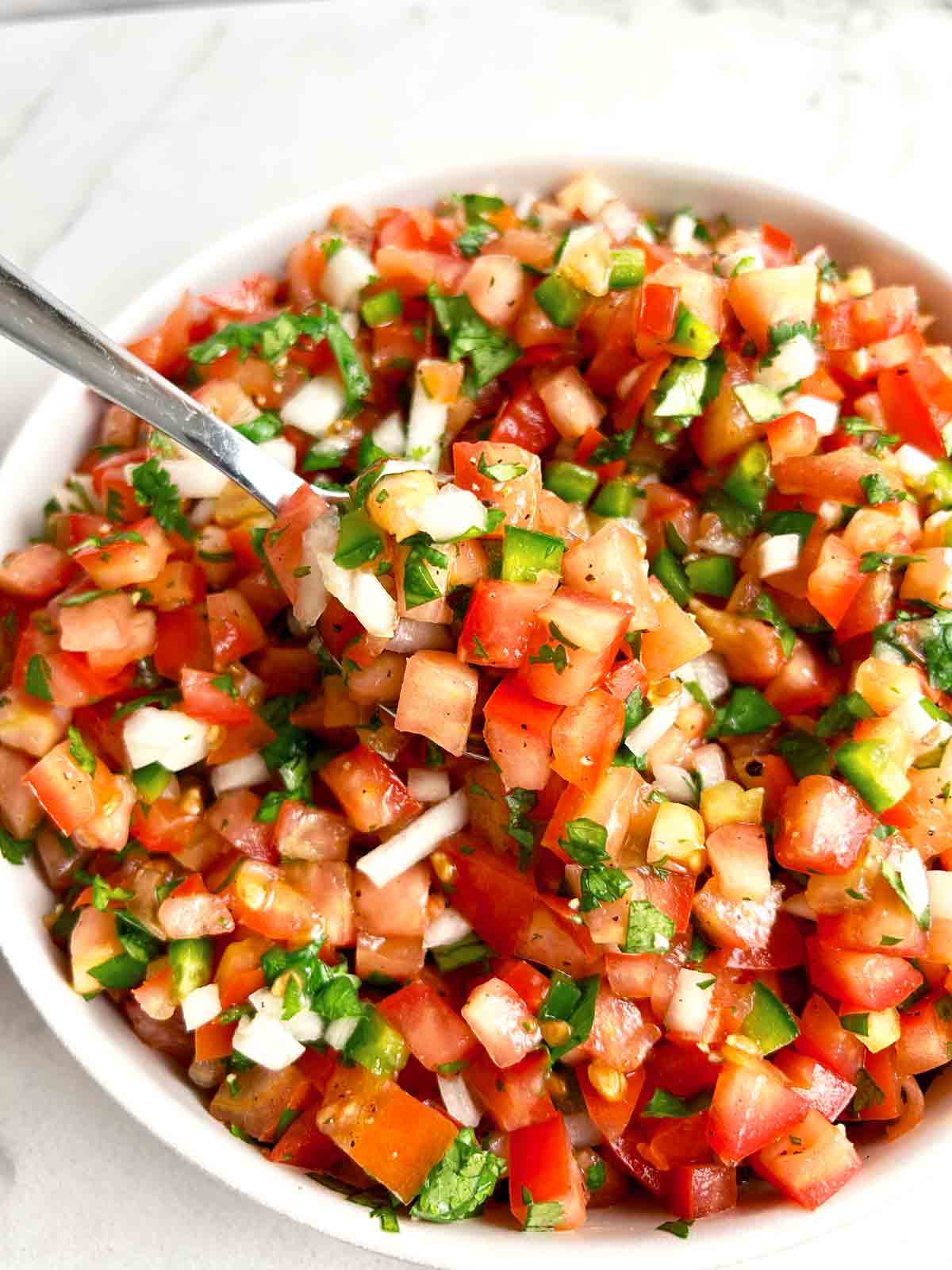 spoon lifting pico de gallo from bowl.