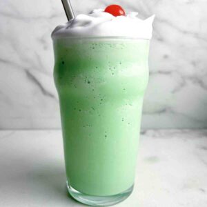 tall glass of shamrock shake with cream and cherry on top.