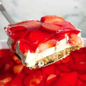 spatula lifting slice of strawberry pretzel salad from dish.