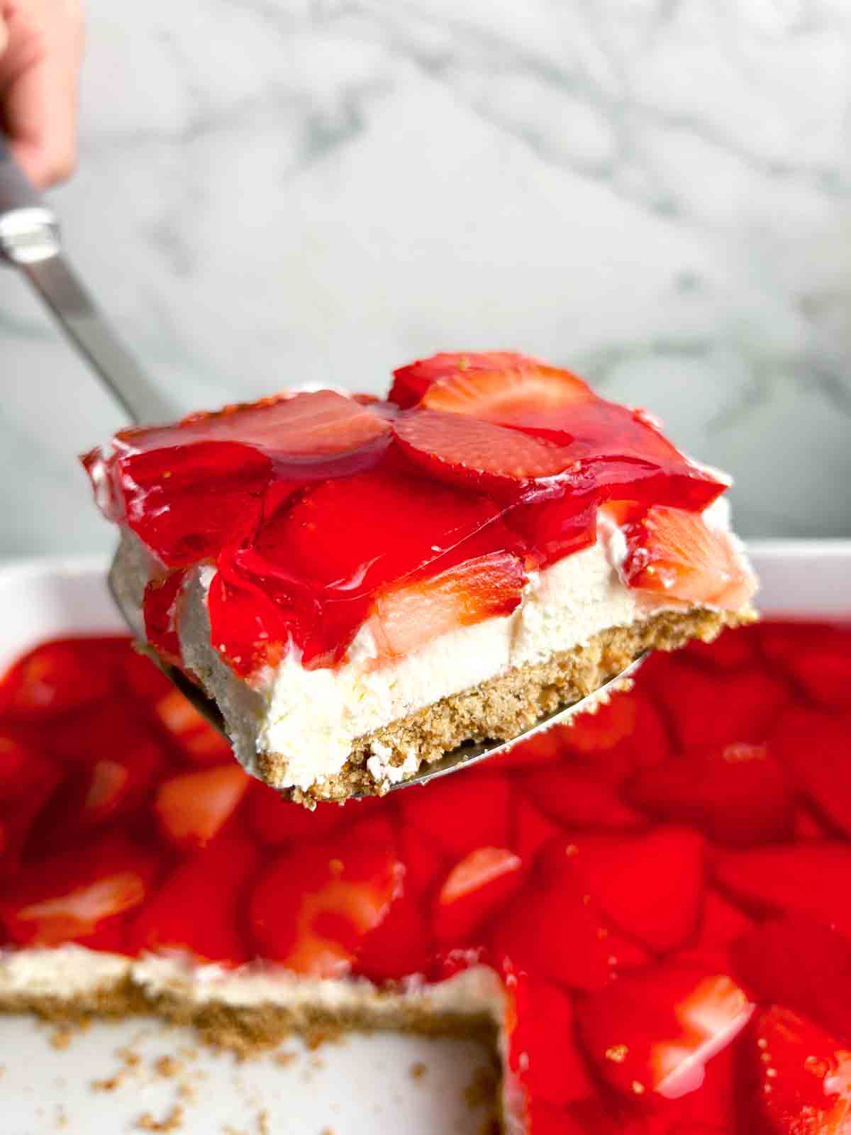 spatula lifting slice of strawberry pretzel salad from dish.