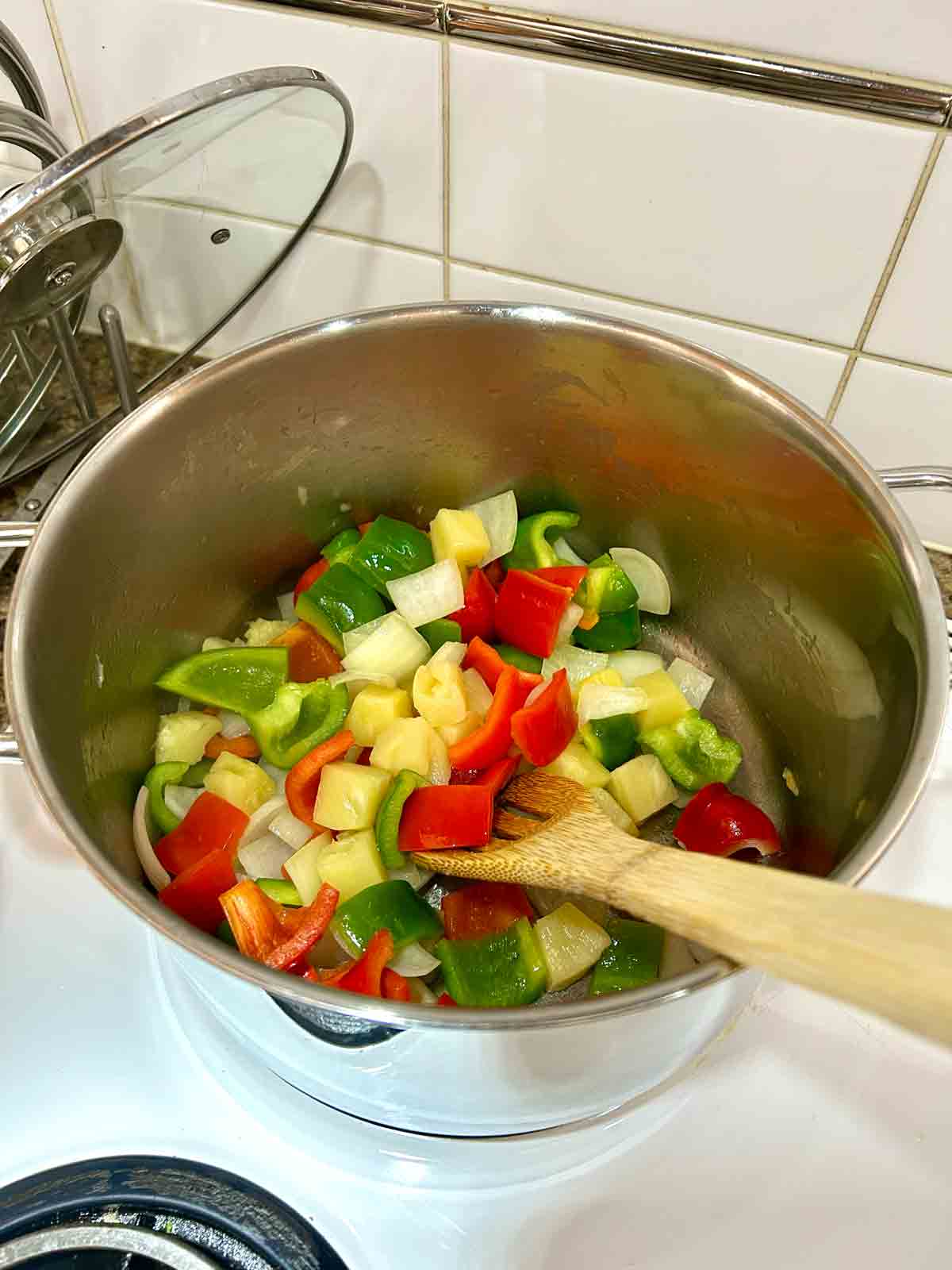 pineapple, onions, and bell peppers being cooked in large pot.
