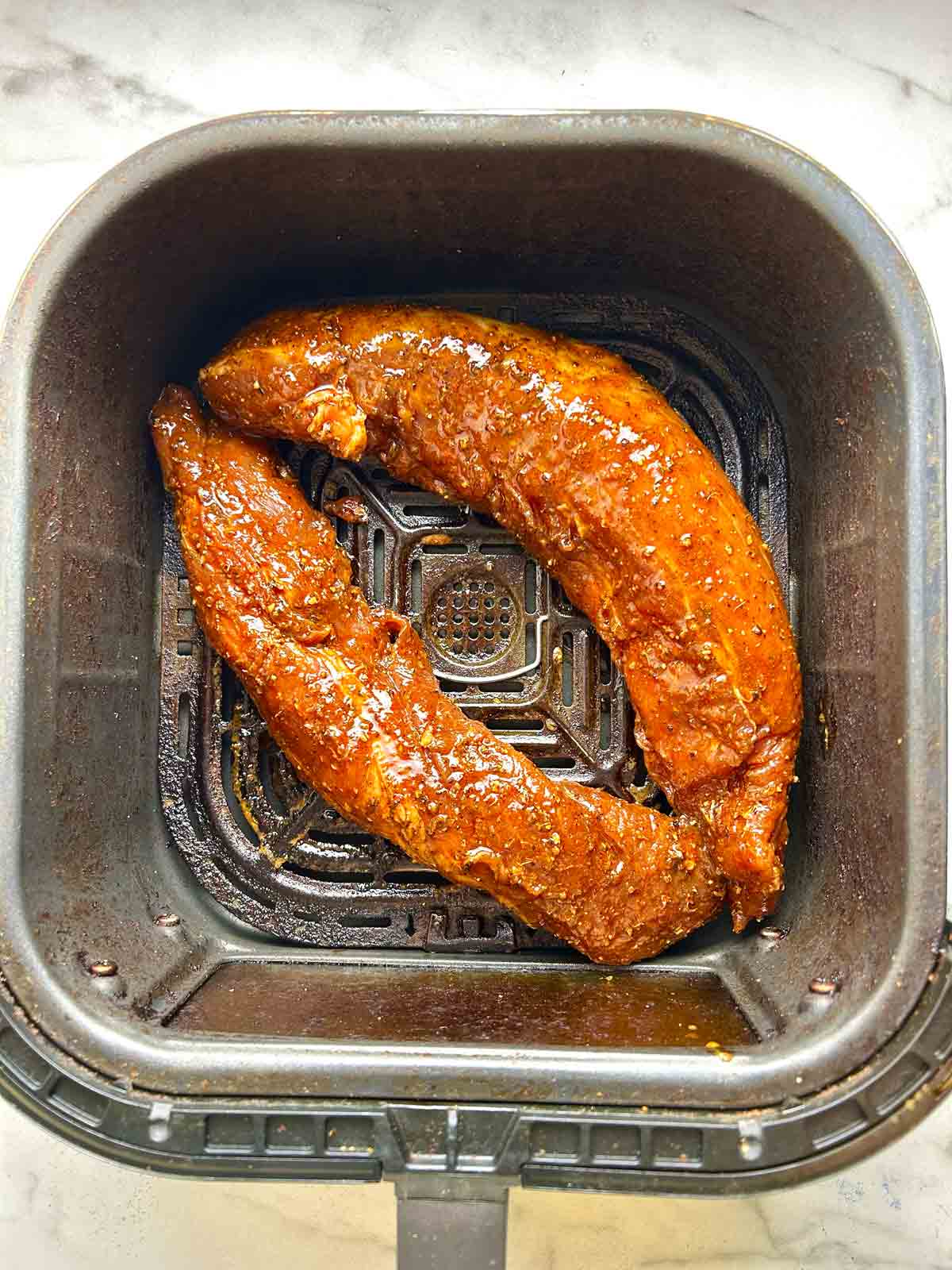seasoned pork tenderloins arranged in air fryer basket.