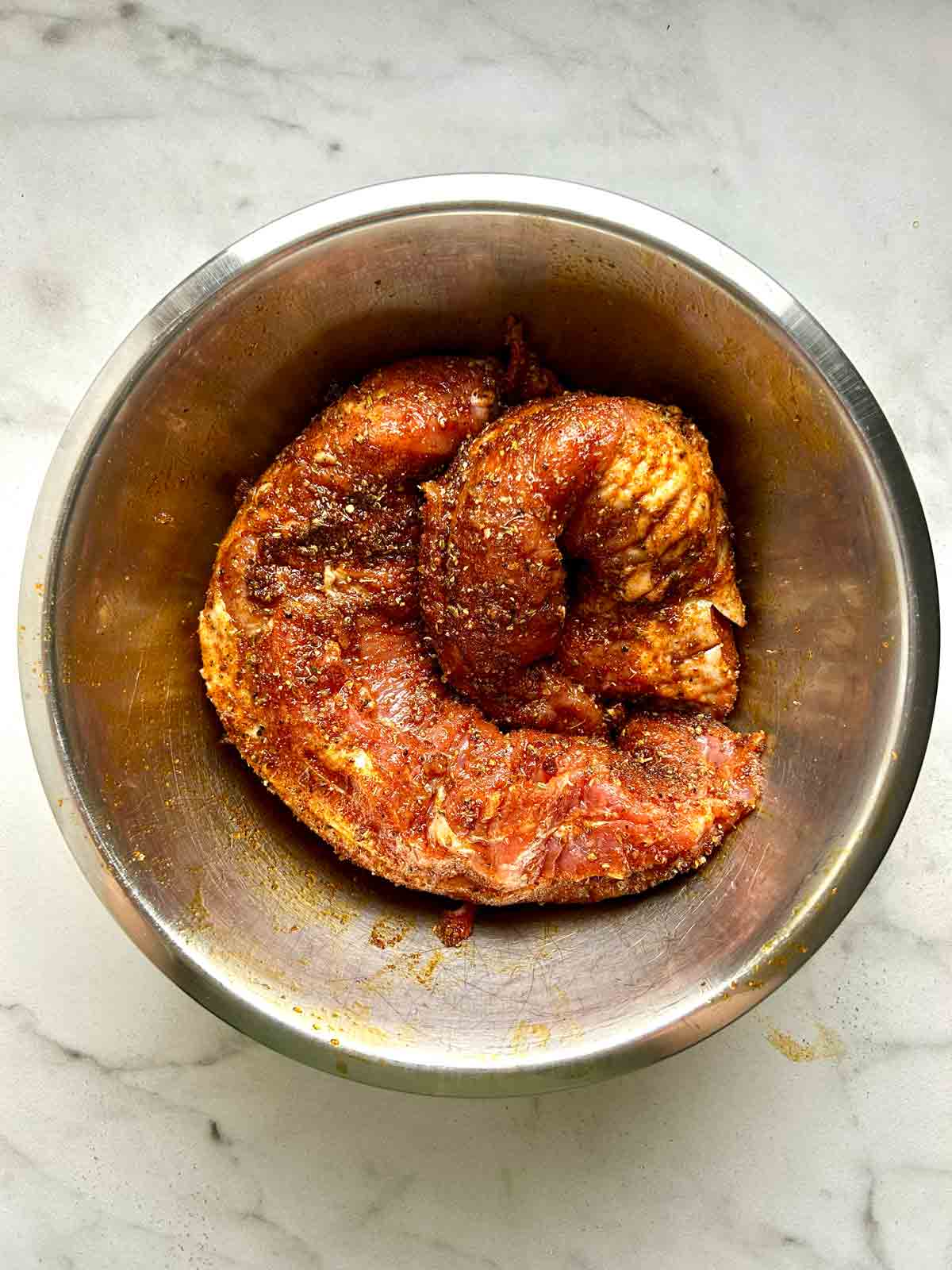 pork tenderloins massaged with spice rub in bowl.