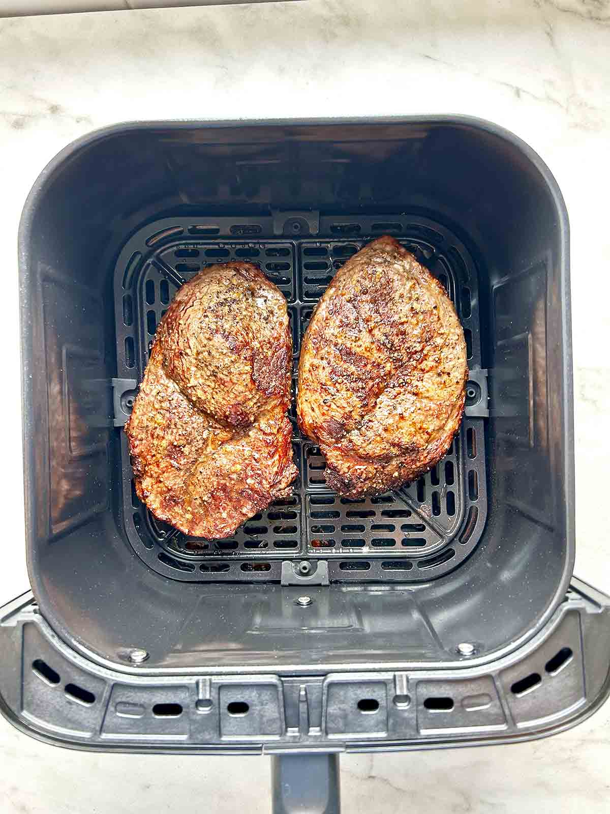 steaks in air fryer basket after being air-fried; golden brown.
