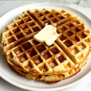 close up of 2 almond flour waffles with syrup and a pat of butter on top.