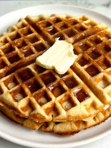 close up of 2 almond flour waffles with syrup and a pat of butter on top.