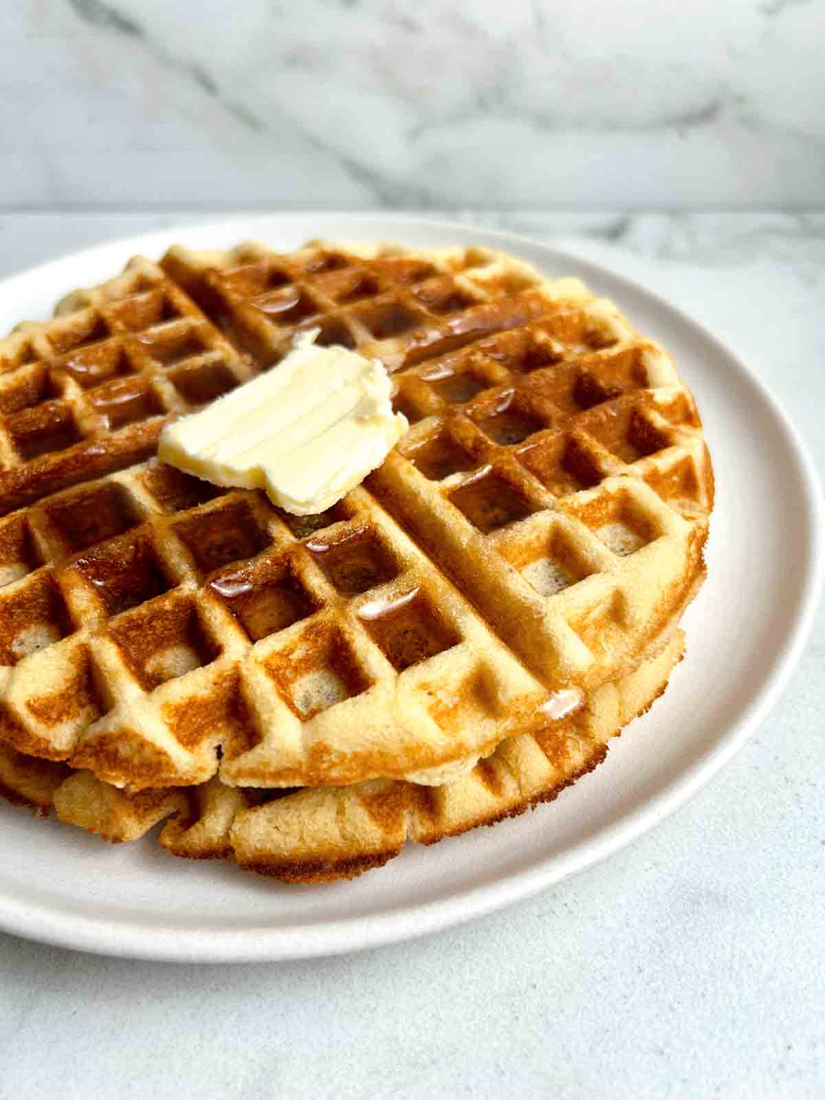 close up of 2 almond flour waffles with syrup and a pat of butter on top.