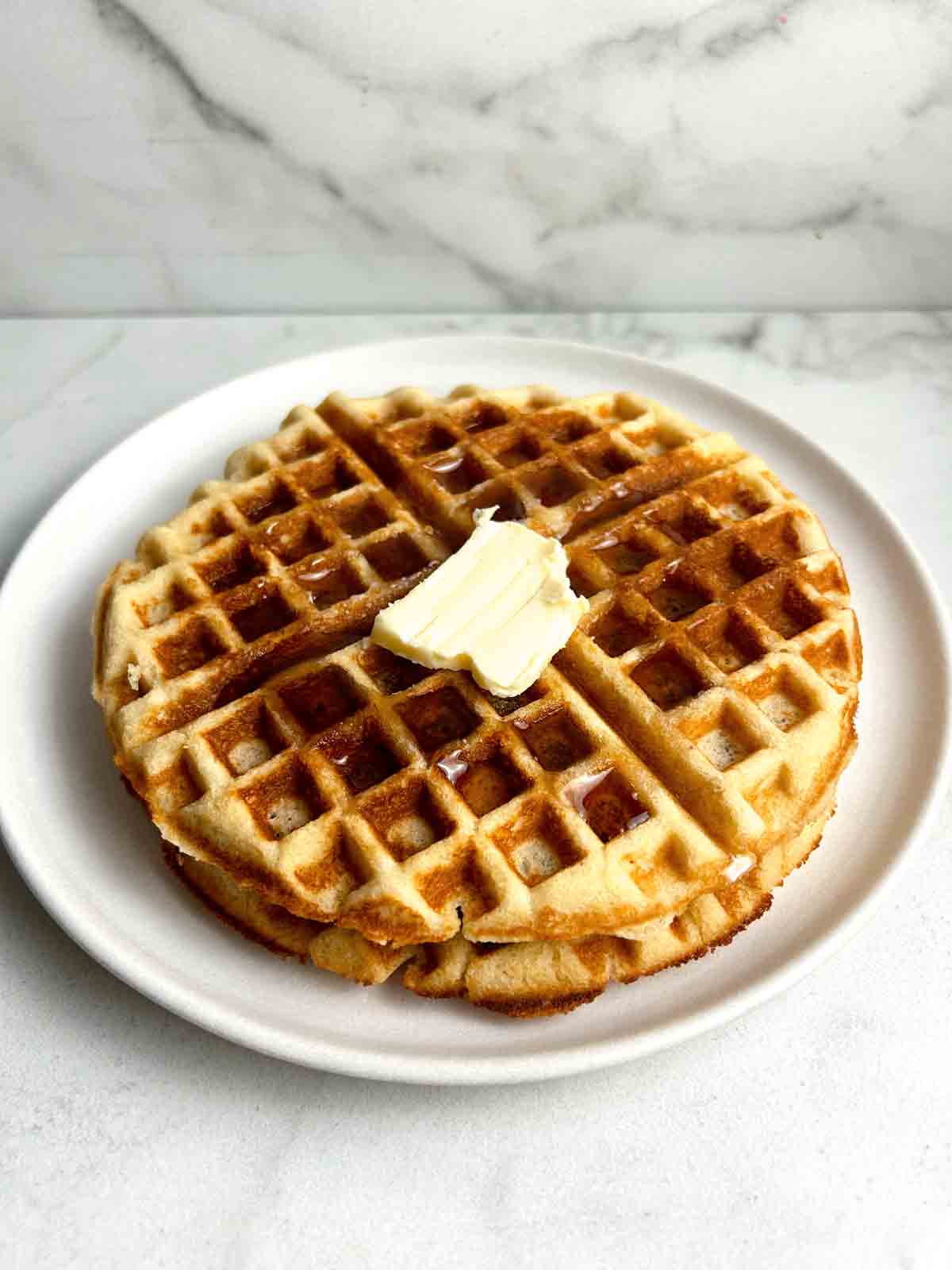 close up of 2 almond flour waffles with syrup and a pat of butter on top.