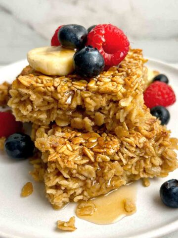two slices of baked oatmeal on top of each other; maple syrup drizzled on top and fresh berries on plate.