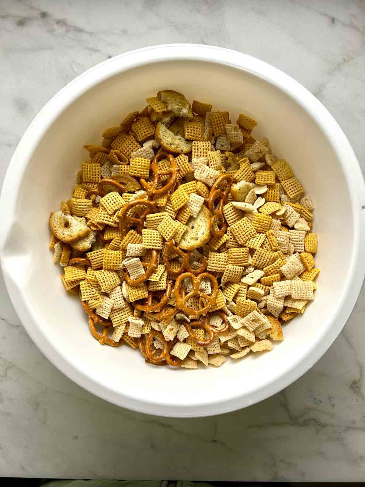 cereals, pretzels, bagel chips, and nuts tossed together in large bowl.