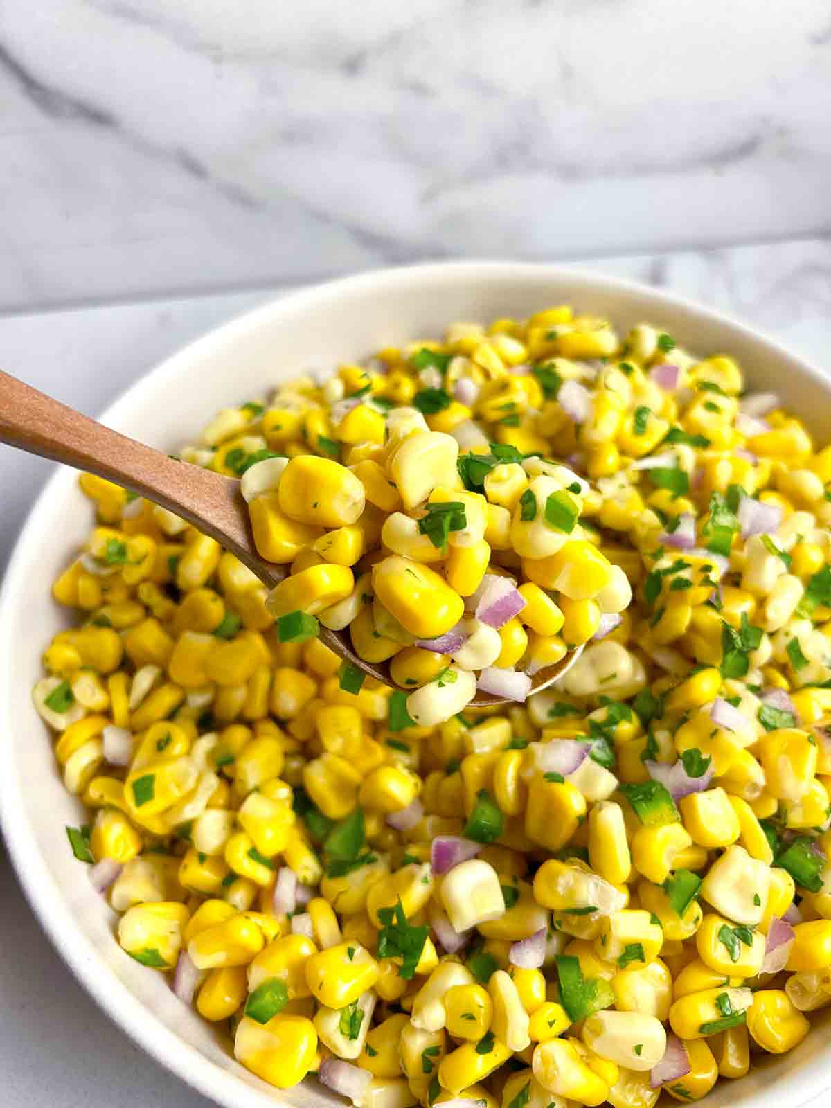 wooden spoon lifting corn salsa from white bowl.