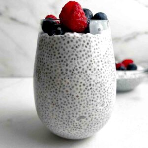 close up of coconut chia pudding in glass cup; fresh raspberries and blueberries on top.