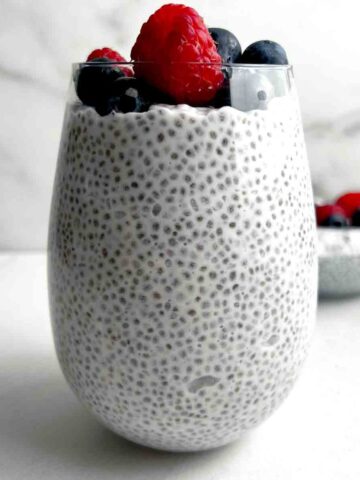 close up of coconut chia pudding in glass cup; fresh raspberries and blueberries on top.