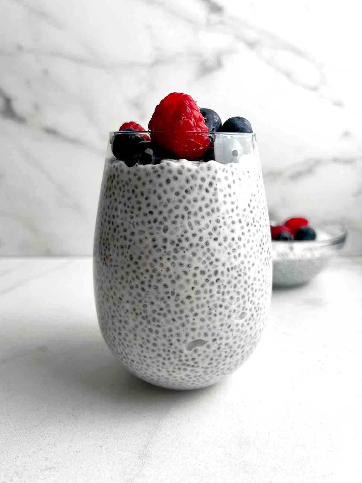 close up of coconut chia pudding in glass cup; fresh raspberries and blueberries on top.