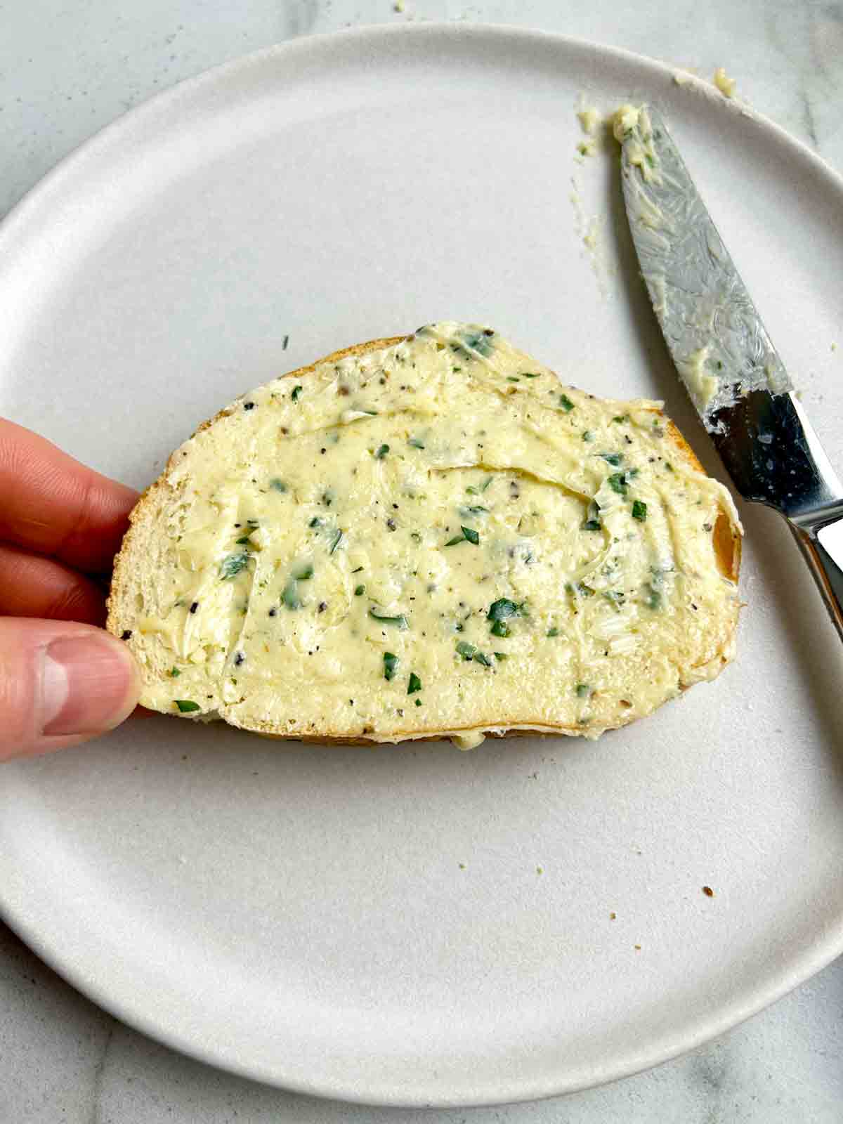 handing holding piece of bread spread with garlic butter.