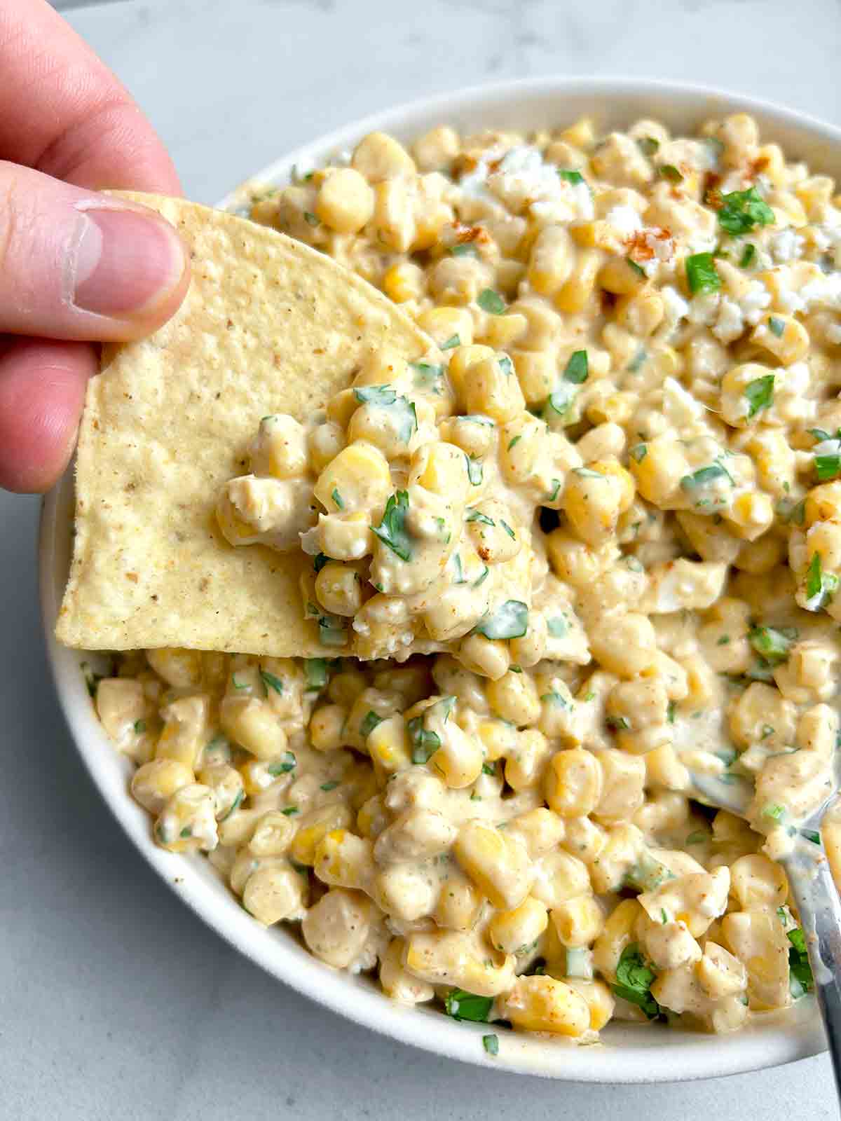 tortilla chip scooping corn dip from bowl.