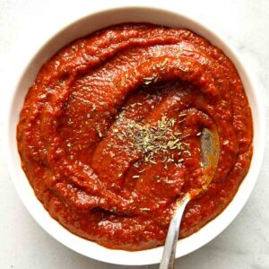 bowl of pizza sauce with dried herbs sprinkled on top and spoon in it.